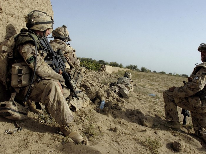 Soldiers in camouflage resting near a wall