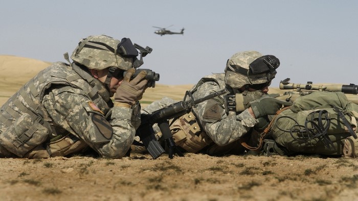 Soldiers aiming rifles with helicopter in background