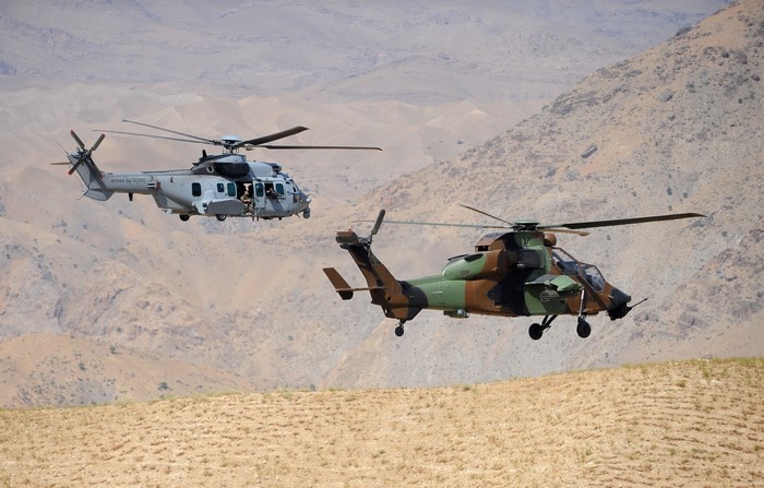 Two military helicopters flying over a desert landscape