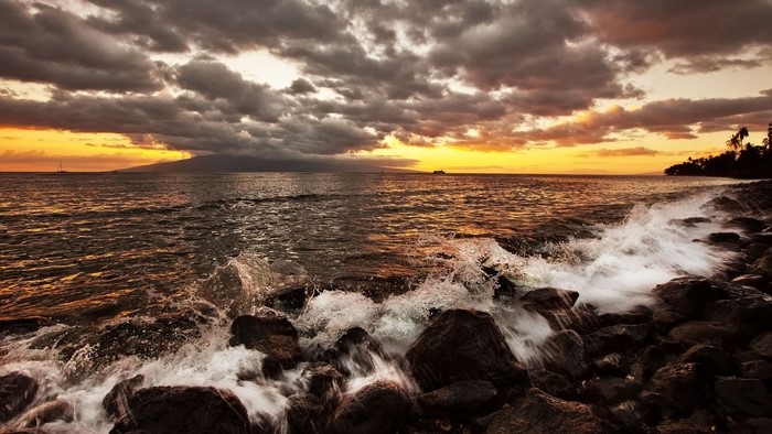 Sunset over the ocean with waves crashing on rocks