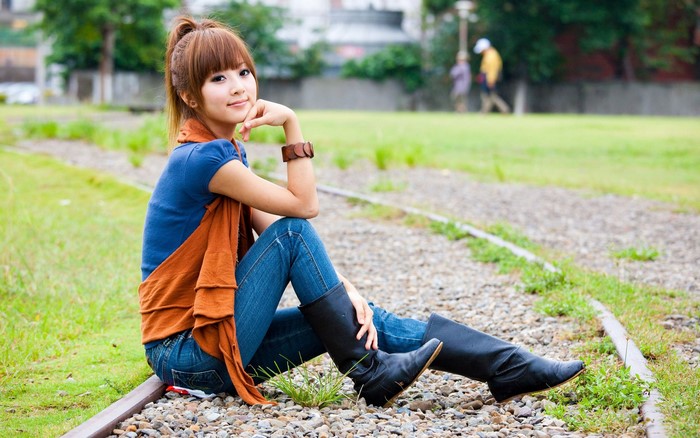 Asian woman wearing boots sitting on train tracks