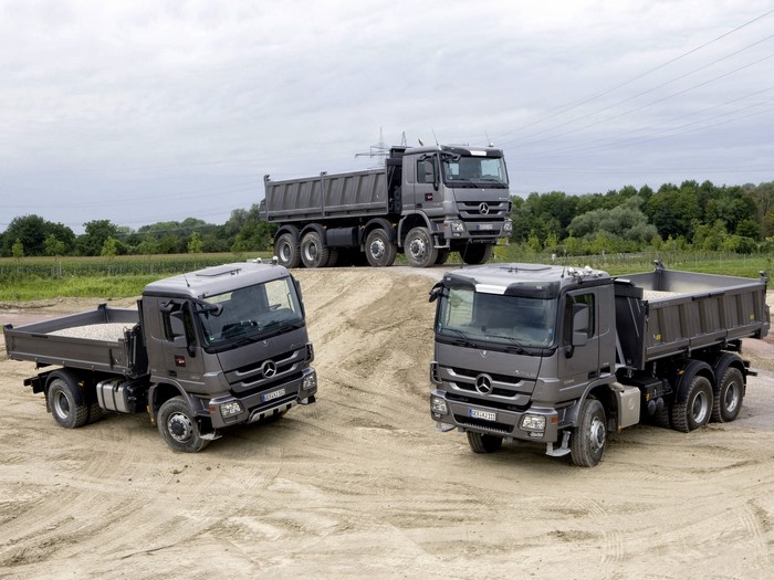 Three Mercedes-Benz dump trucks on a dirt pile