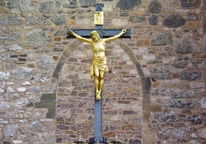 Golden Jesus Christ on a cross in front of a stone wall