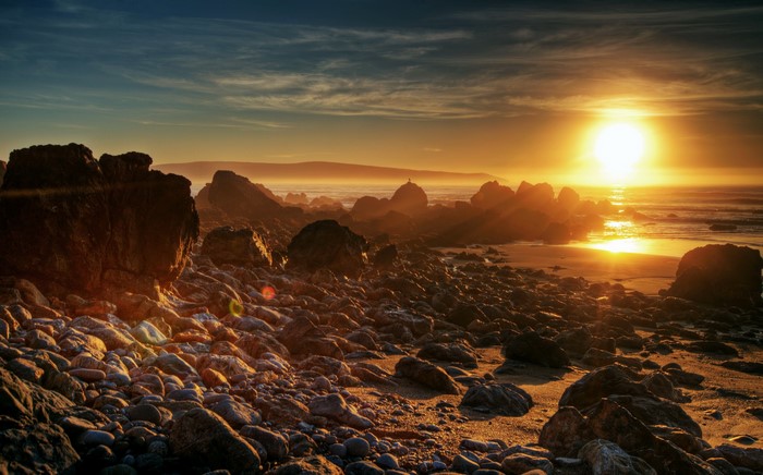 Sunset over a rocky beach with the sun setting over the ocean