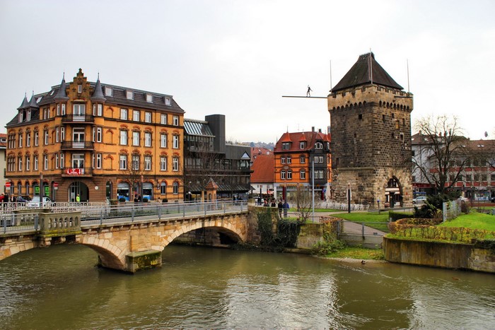 Acrobat on a wire over a river in front of a tower and buildings