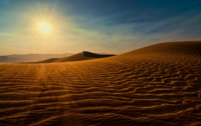 Desert sand dunes at sunset with sun and mountains