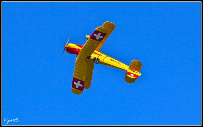 Yellow biplane with Swiss cross insignia flying in blue sky