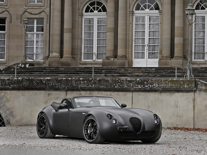 Matte black Wiesmann convertible sports car in front of a mansion