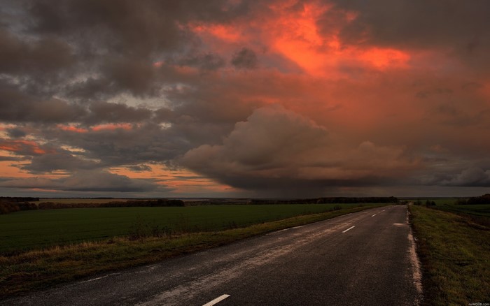 Road through a field under a dramatic sunset sky
