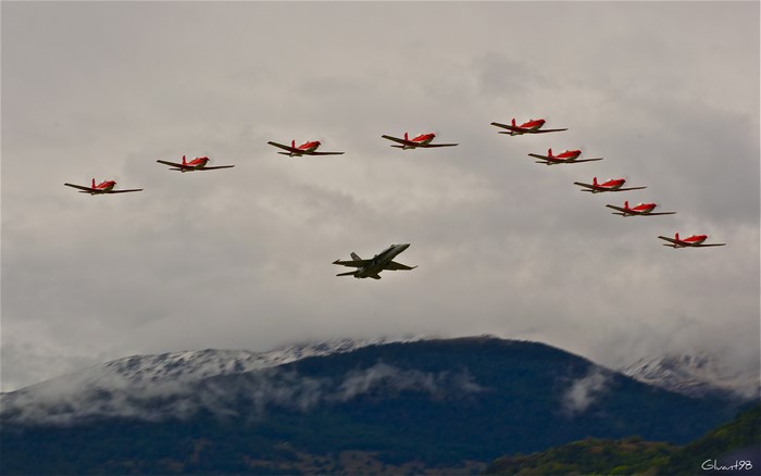 Fighter jet flies with formation of red propeller planes