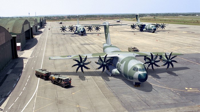 Military transport planes parked on tarmac with hangars