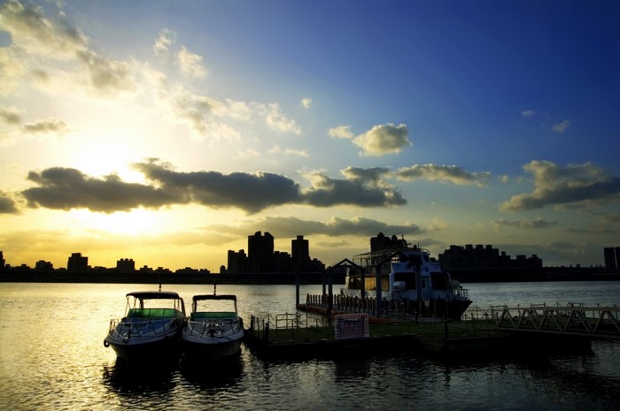 Boats docked on a river at sunset with city skyline