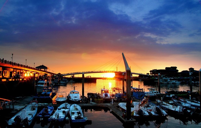 Boats docked at a harbor during sunset with a bridge