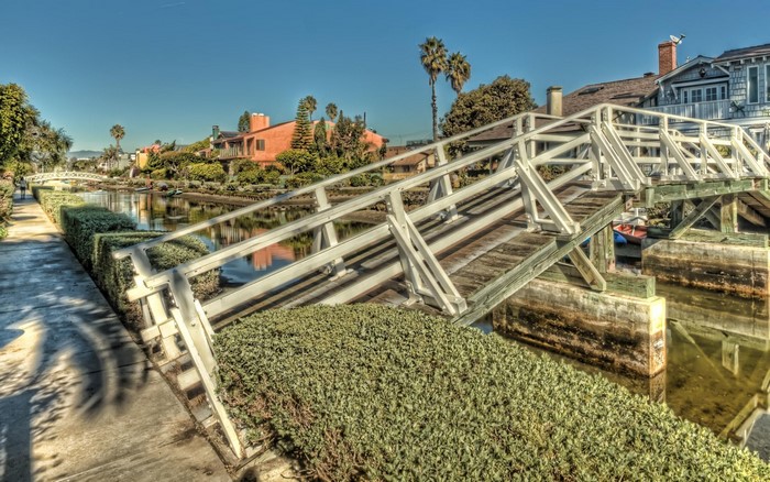 White wooden bridge over a canal with houses and palm trees