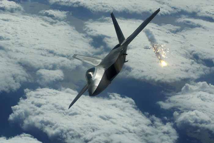 Fighter jet fires a flare over clouds