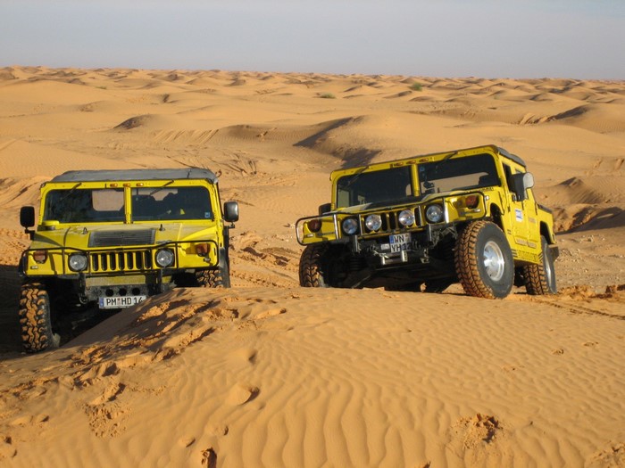Two yellow Hummers driving on sand dunes
