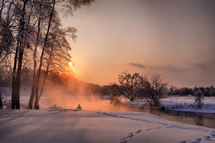 Winter sunrise over a misty river with snow-covered trees