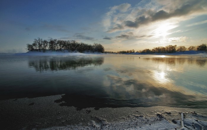 Sunrise over a frozen river with trees and mist