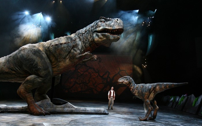 Two Tyrannosaurus Rex dinosaurs and a man on stage
