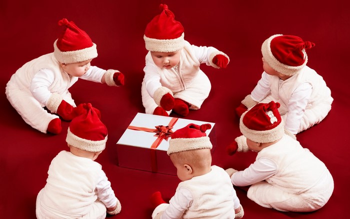Babies in Santa hats around a Christmas gift