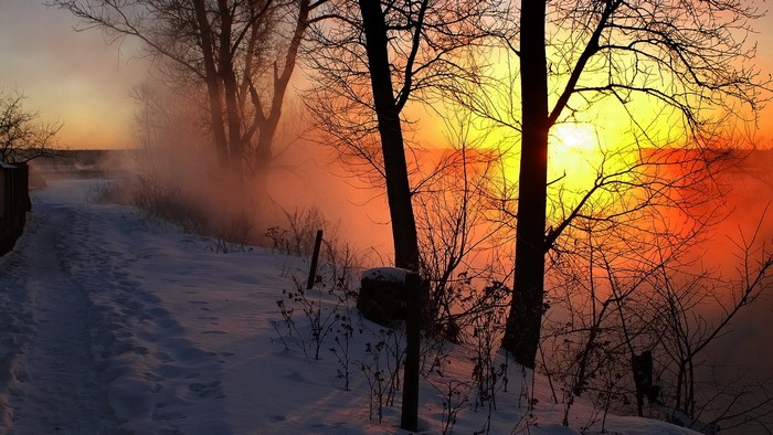 Winter sunrise over a misty river with snow-covered path