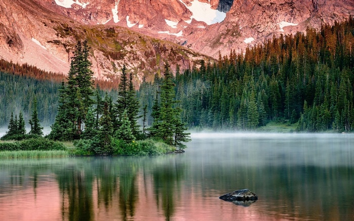 Misty mountain lake with pine forest and rocky peaks