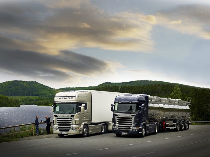 Two Scania trucks on a road with a lake and mountains