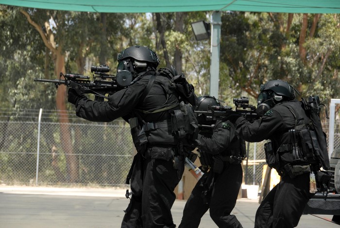 Soldiers in black tactical gear with gas masks and rifles