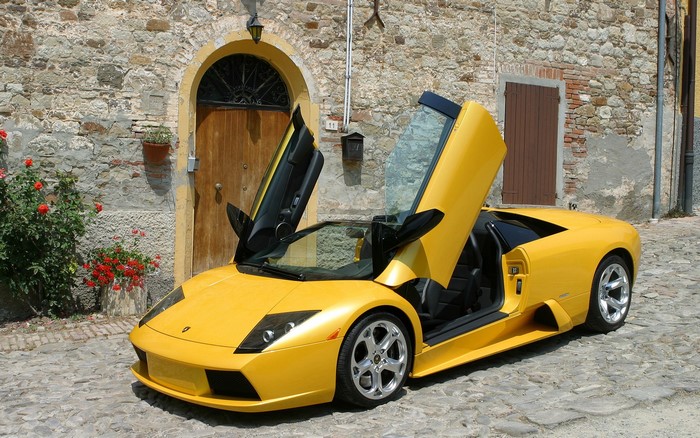 Yellow Lamborghini with doors open in front of stone building