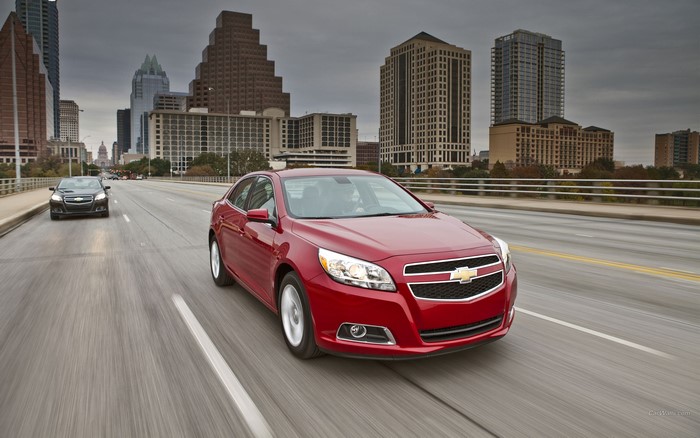 Red Chevrolet Malibu driving on a city bridge