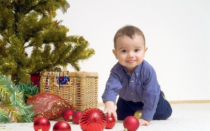 Baby boy playing with Christmas ornaments near a tree