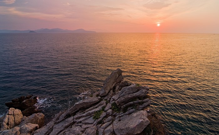 Sunset over the ocean with rocky shore