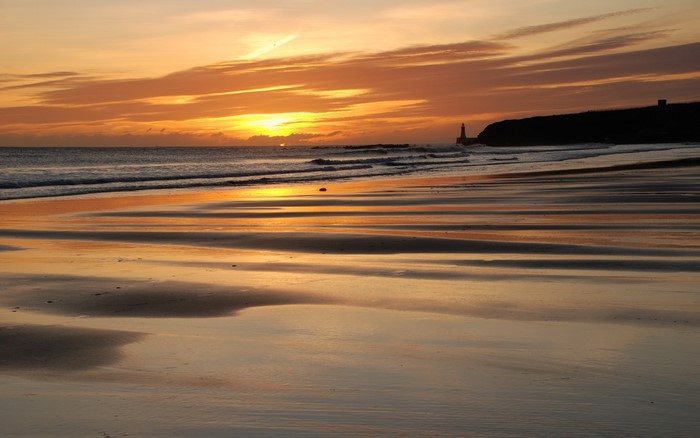 Sunset over a beach with a lighthouse