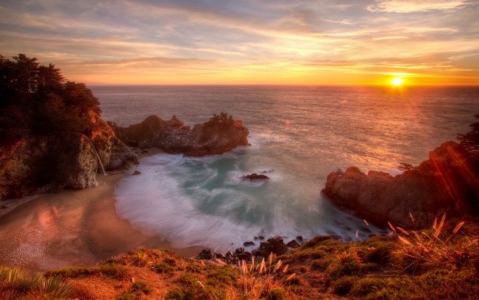 Sunset over a rocky coastline with a waterfall