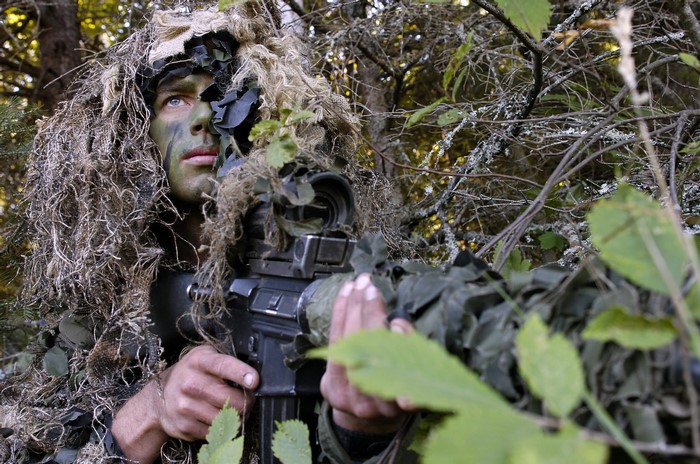 Soldier in camouflage aiming a rifle in a forest
