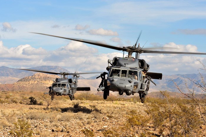 Two military helicopters flying over a desert landscape