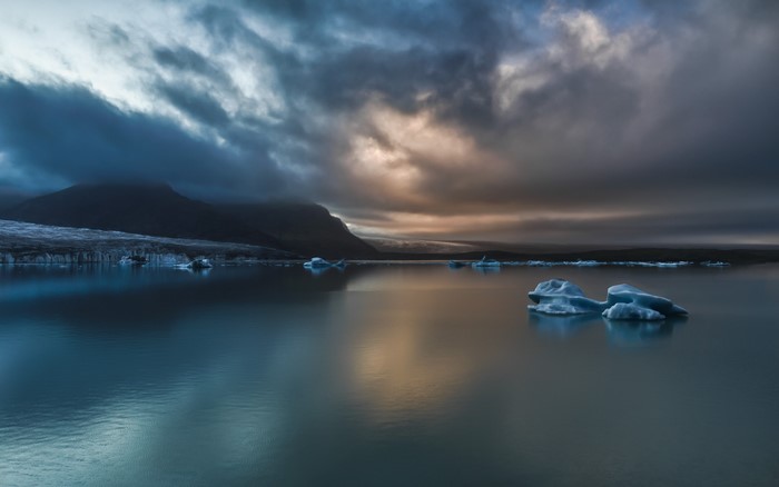 Icebergs in a lake with mountains and dramatic clouds