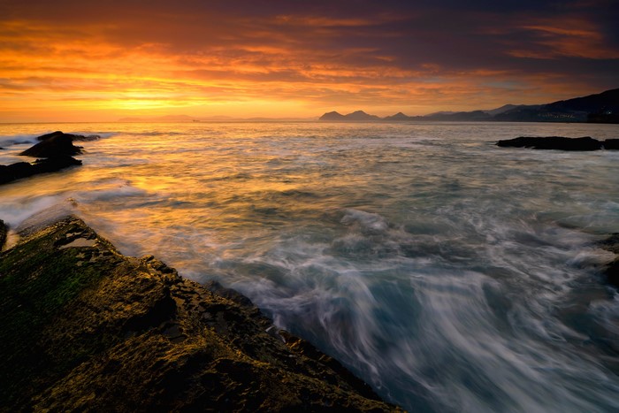 Ocean waves crashing on rocks at sunset