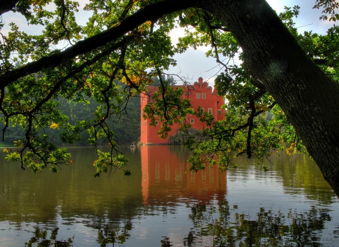 Red castle reflected in water, framed by trees