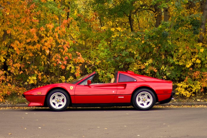 Red Ferrari convertible parked on a street with autumn trees
