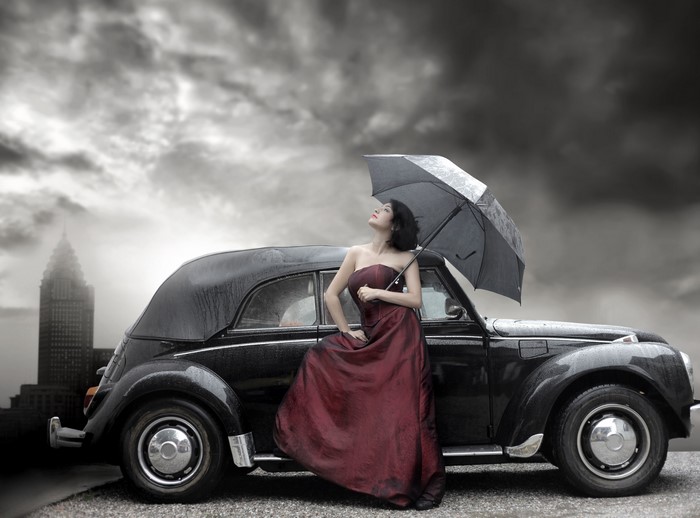 Woman in red dress with umbrella by vintage car