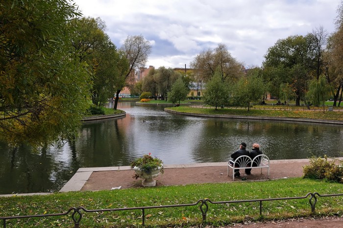 People sitting on a bench in a park by a pond