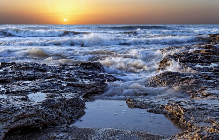 Sunset over the ocean with waves crashing on rocks