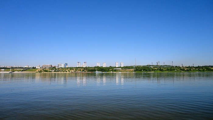 City skyline across a wide river under a clear blue sky