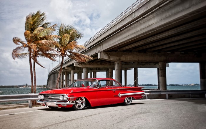 Red Chevrolet parked under a bridge with palm trees