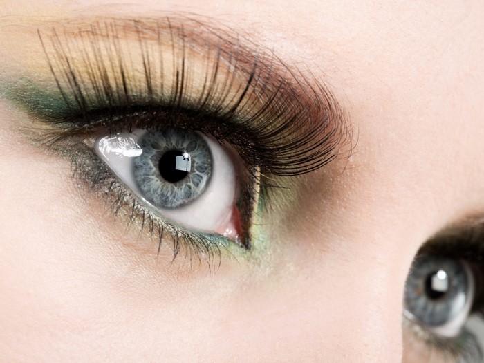 Close-up of a woman's blue eye with green eyeshadow and false eyelashes