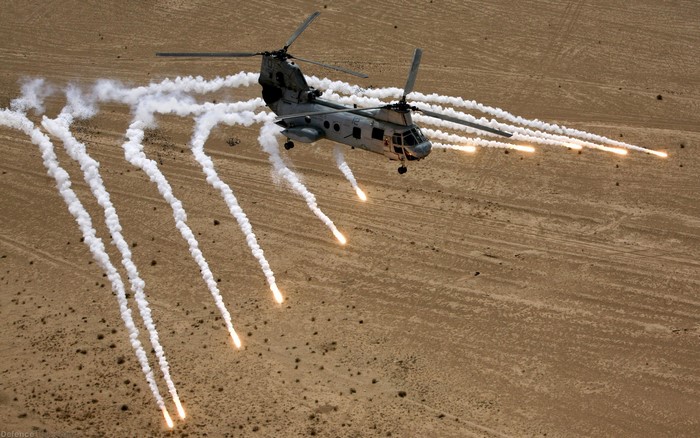 Helicopter deploying flares over desert terrain