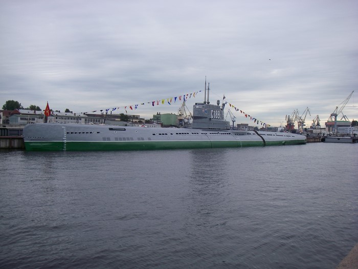 Submarine C189 docked in a harbor with cranes
