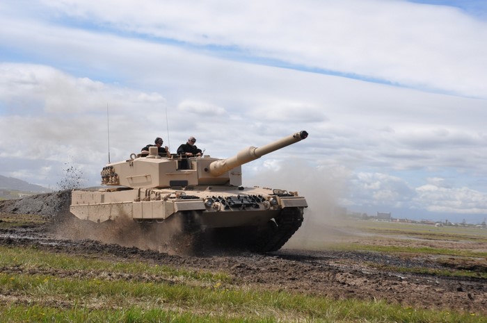Tan tank with two crew members driving off-road