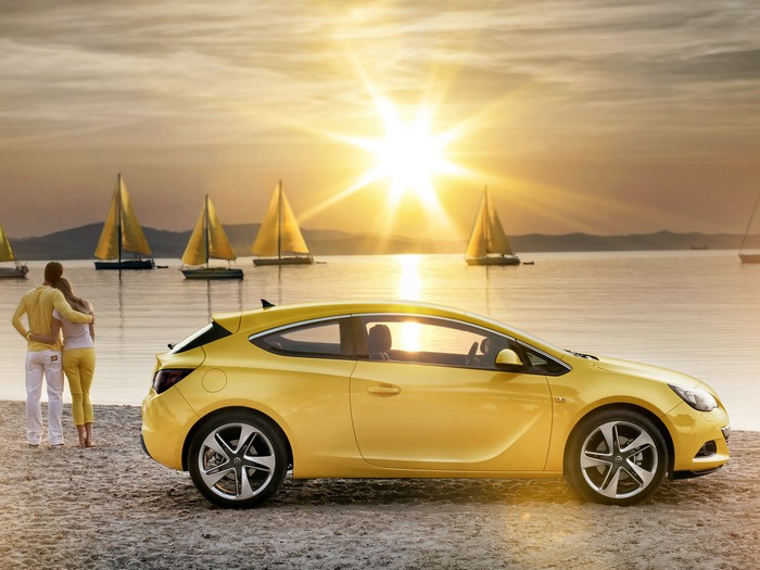 Yellow Opel Astra on a beach with sailboats at sunset
